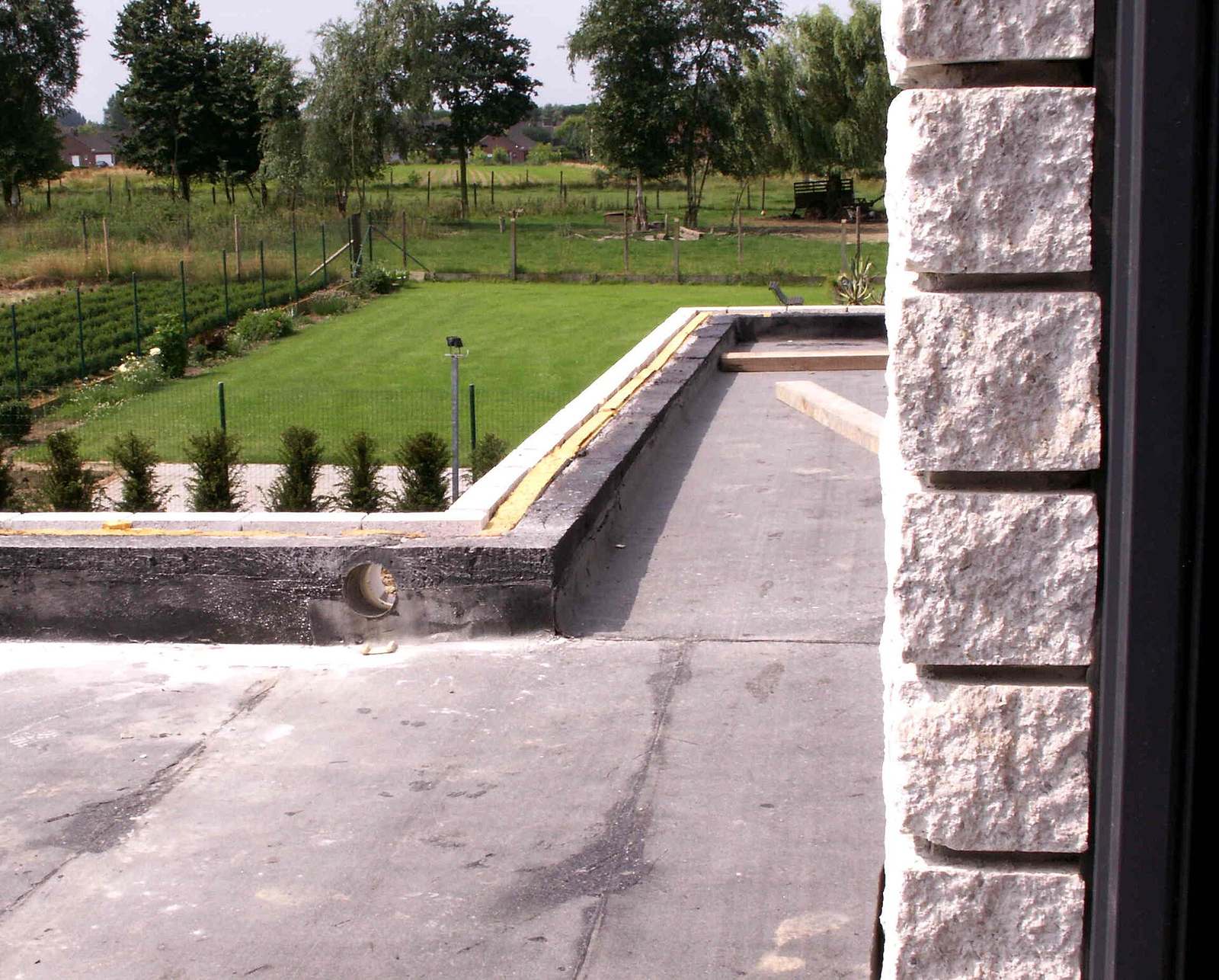 Plat dak met een donkere dakbedekking en een dakrand, uitkijkend op een tuin