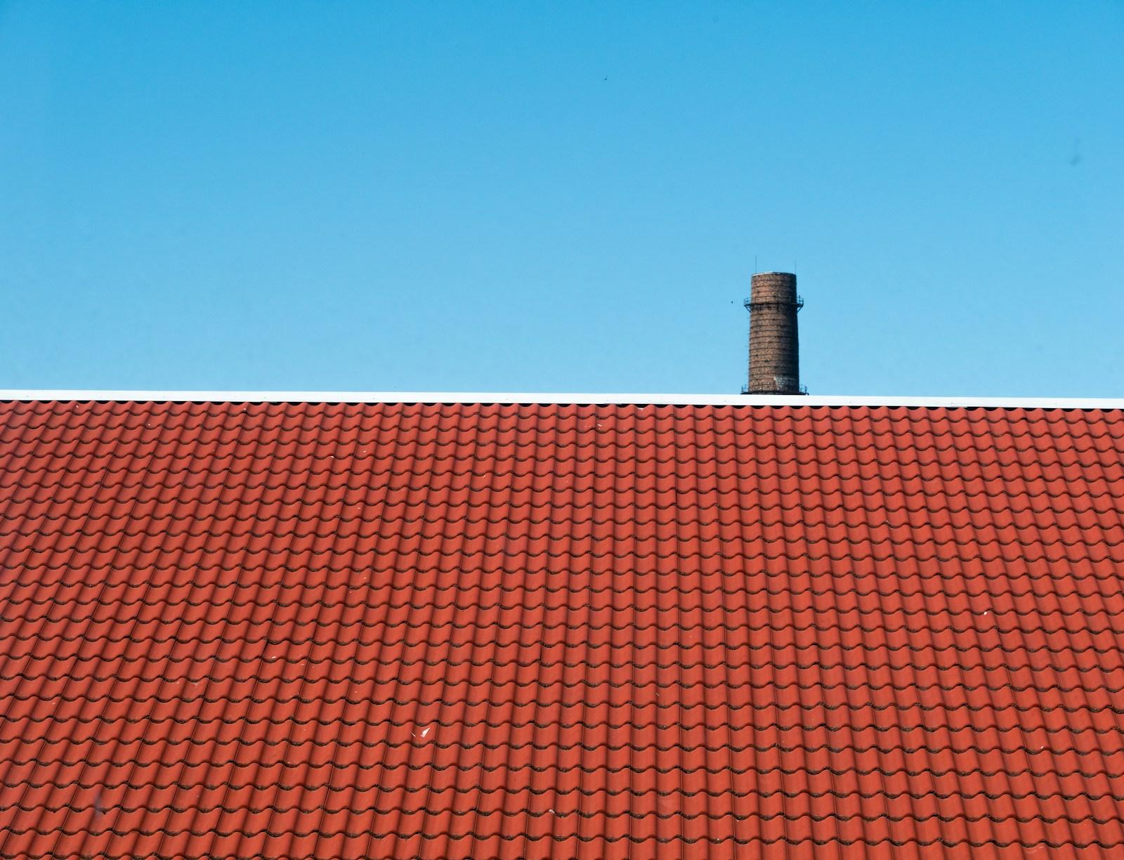 Rood pannendak met een schoorsteen tegen een heldere lucht